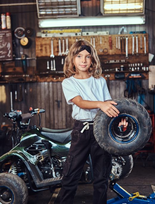 Nice small girl is posing for photographer with big wheel from car at auto service.